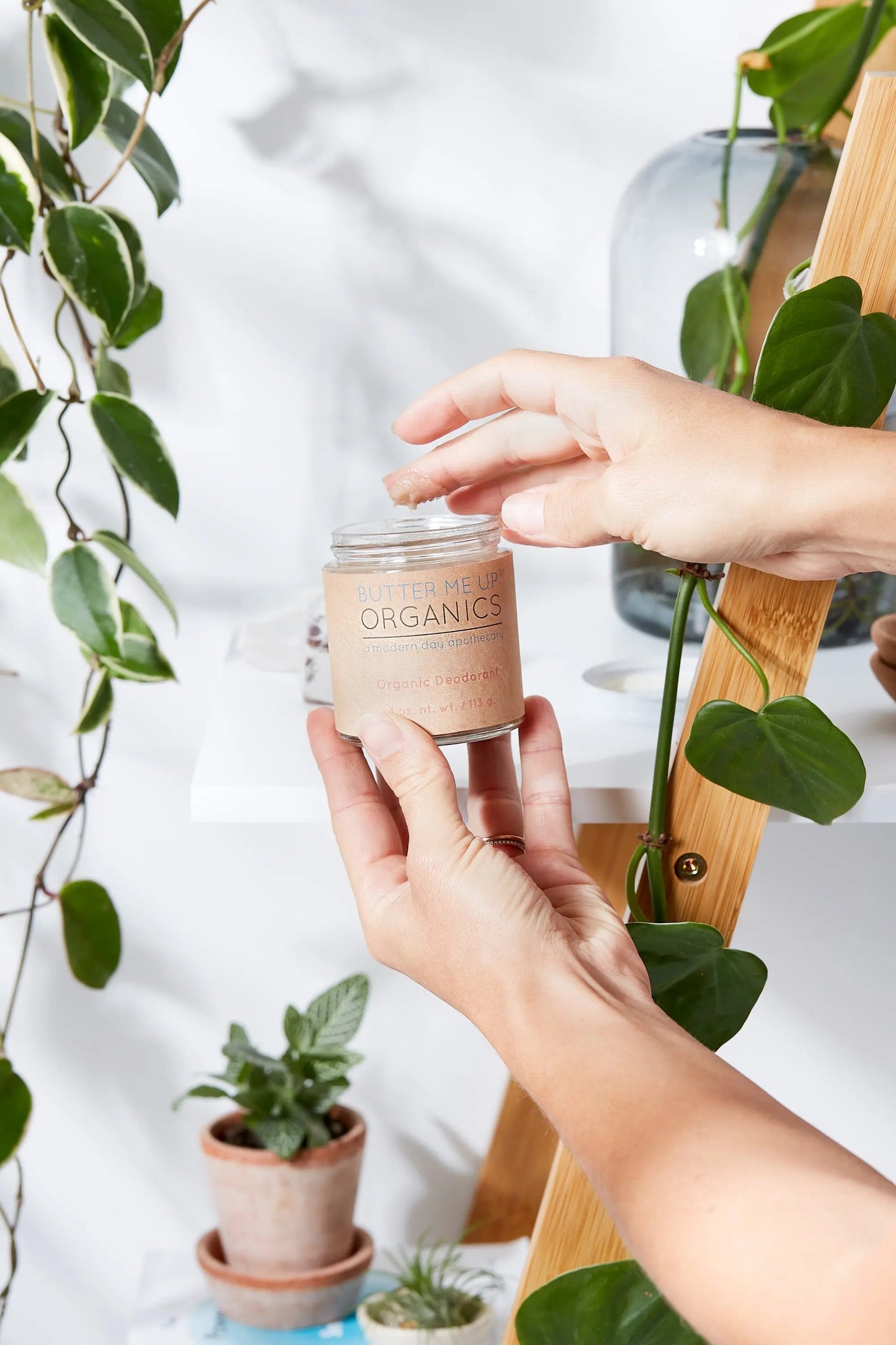 Hand holding a jar of Butter Me Up Organics aluminum-free organic deodorant with plants in the background