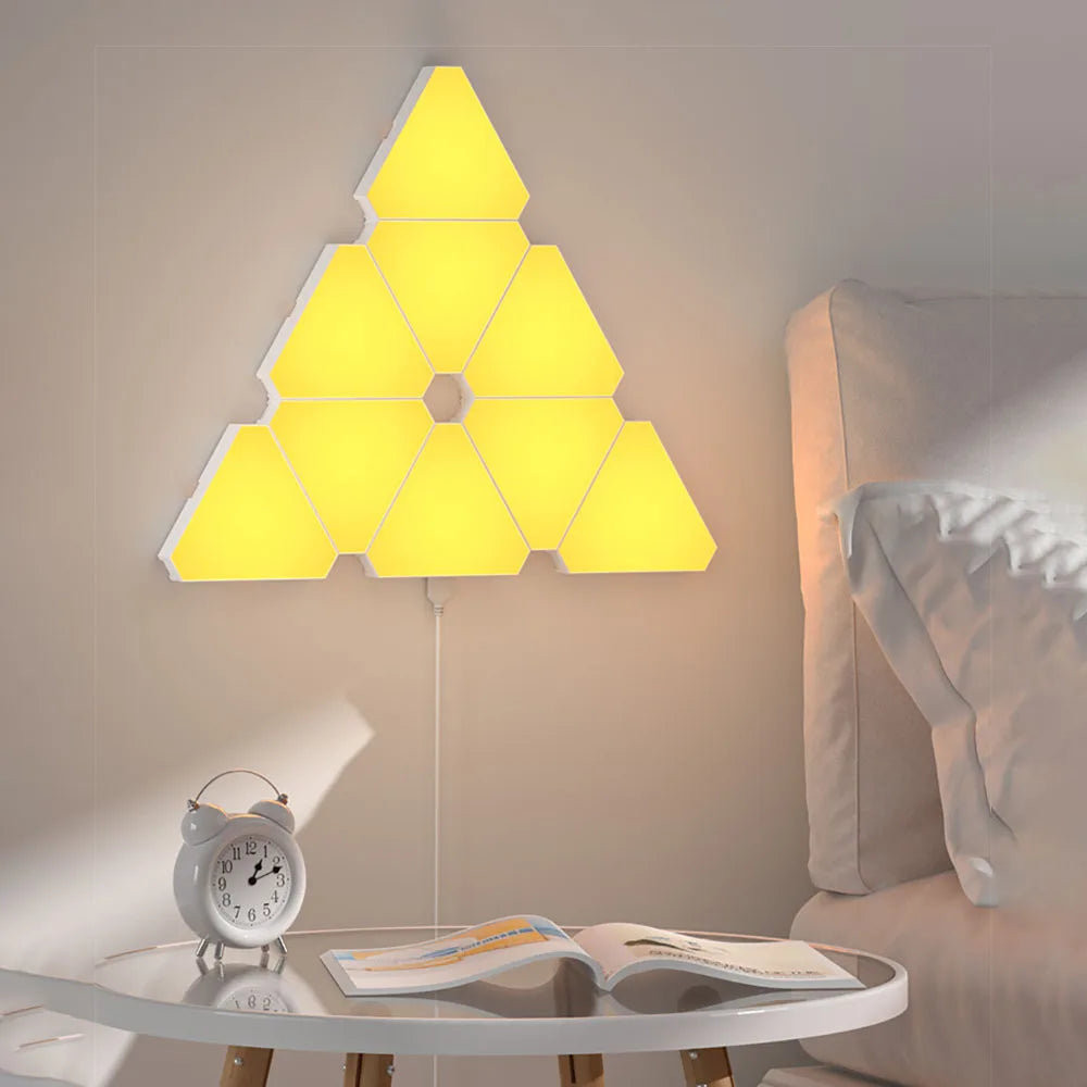 LED Triangular Quantum Lamp glowing yellow mounted on bedroom wall above bedside table with alarm clock and book