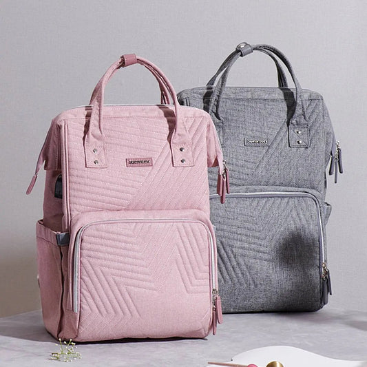 Quilted diaper bag backpack in pink and gray with multiple pockets and padded handles designed for parents on the go