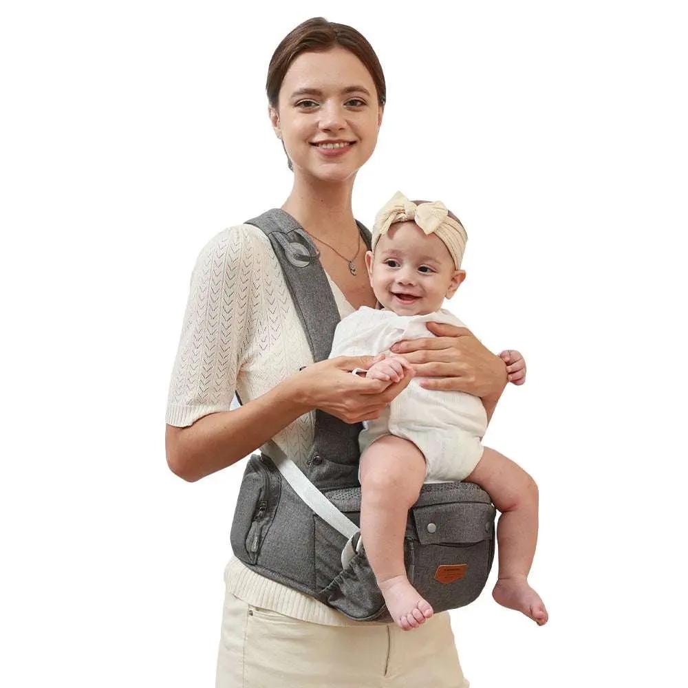 Woman wearing ergonomic baby carrier with hip seat holding smiling baby girl