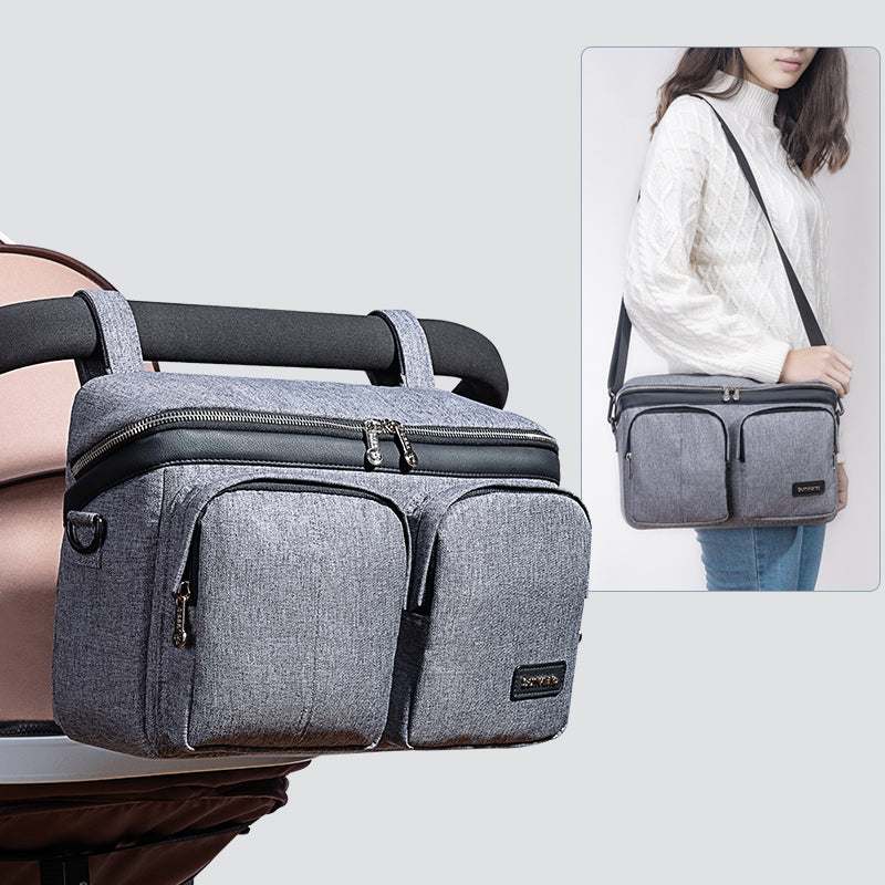 Grey stroller organizer caddy bag with multiple pockets attached to stroller and worn as shoulder bag