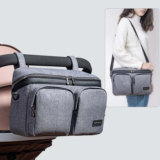 Grey stroller organizer caddy bag with multiple pockets attached to stroller and worn as shoulder bag