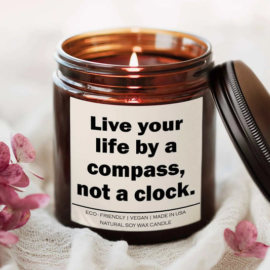 Live your life by a compass not a clock candle in amber jar with lit wick and motivational label