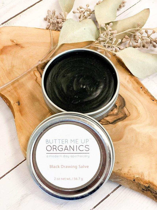 Organic Black Drawing Salve in a tin for bee stings and skin ailments on wooden surface