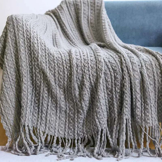 Grey knitted throw blanket with fringe detail draped on sofa for cozy decor