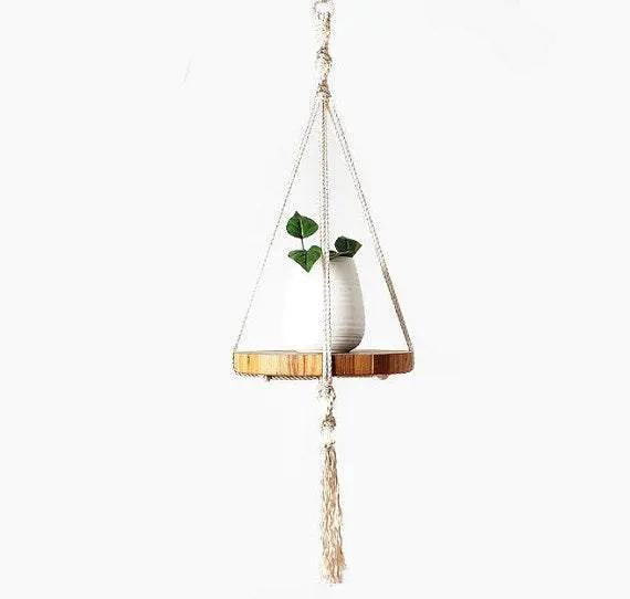 Handcrafted ecru cotton macrame plant hanger with wooden tray holding a small white vase with green leaves
