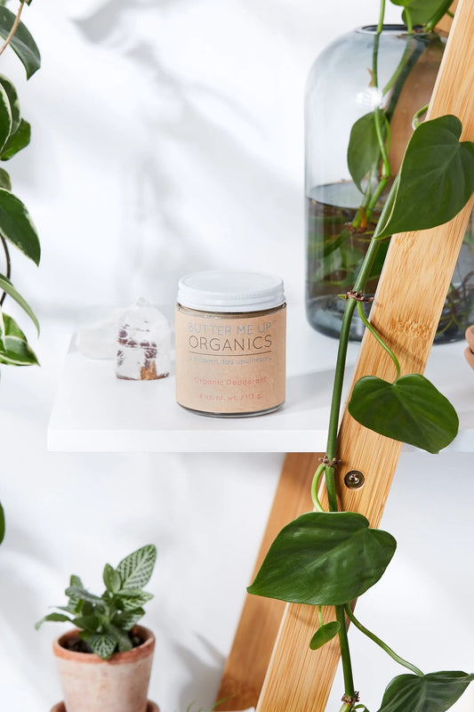 jar of organic deodorant on white shelf with green plants around