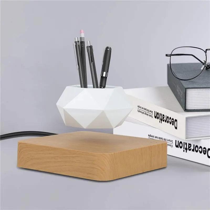 Levitating rotation flowerpot with magnetic floating white geometric pot on wooden base next to books and glasses