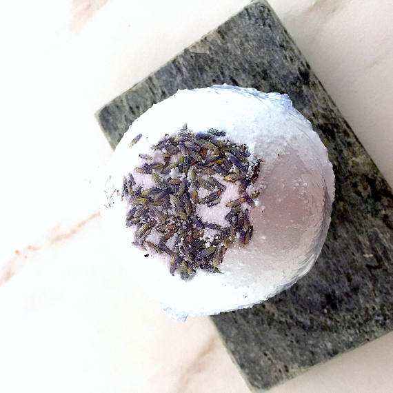 Organic bath bomb with lavender flowers on top, displayed on a stone slab, natural and soothing skincare product