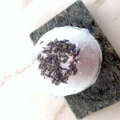 Organic bath bomb with lavender flowers on top, displayed on a stone slab, natural and soothing skincare product